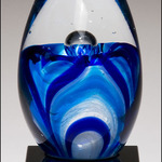 1633-  Art glass egg with blue and white accents on black glass base
